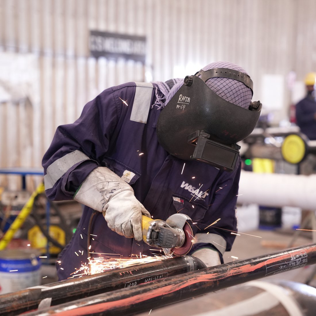 Welder cutting steel pipe, sparks across the frame